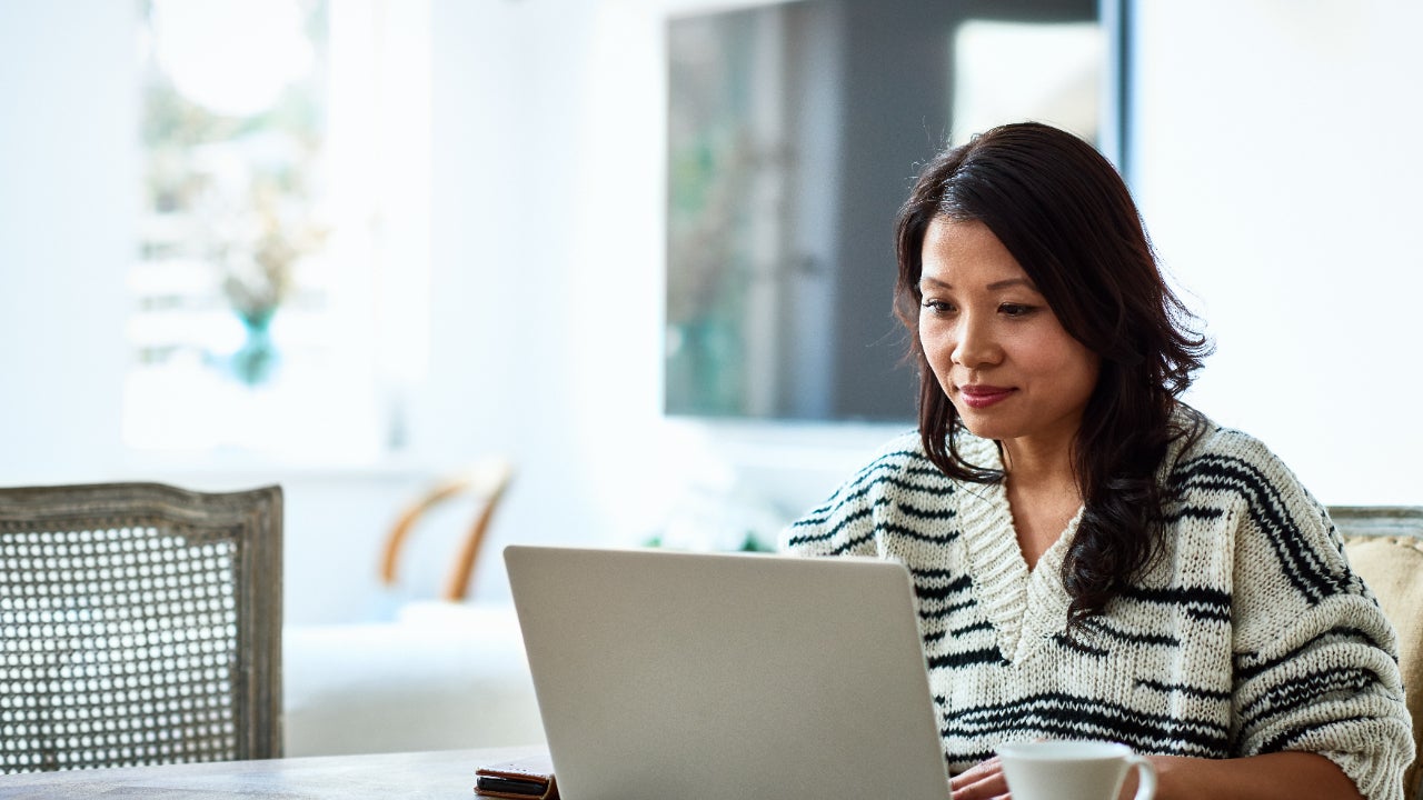 Woman using laptop at table with flat-screen TV in backgroudn