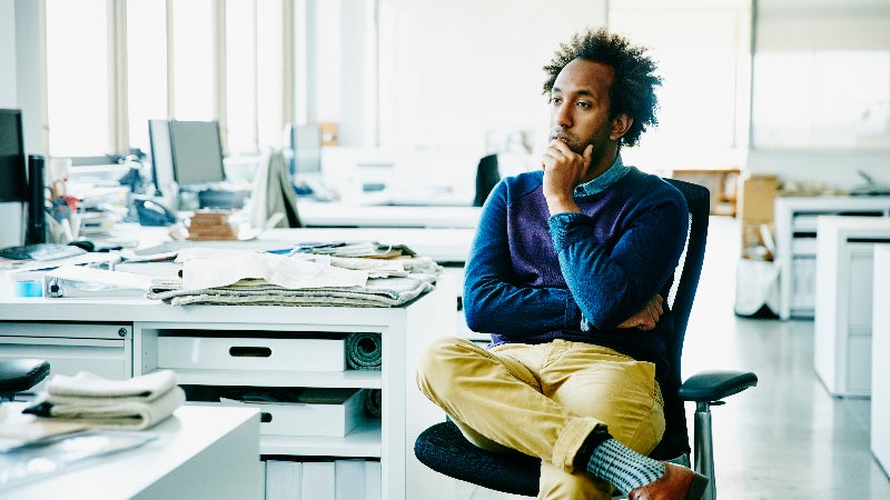 An African-American man sits a work desk with a thoughtful look