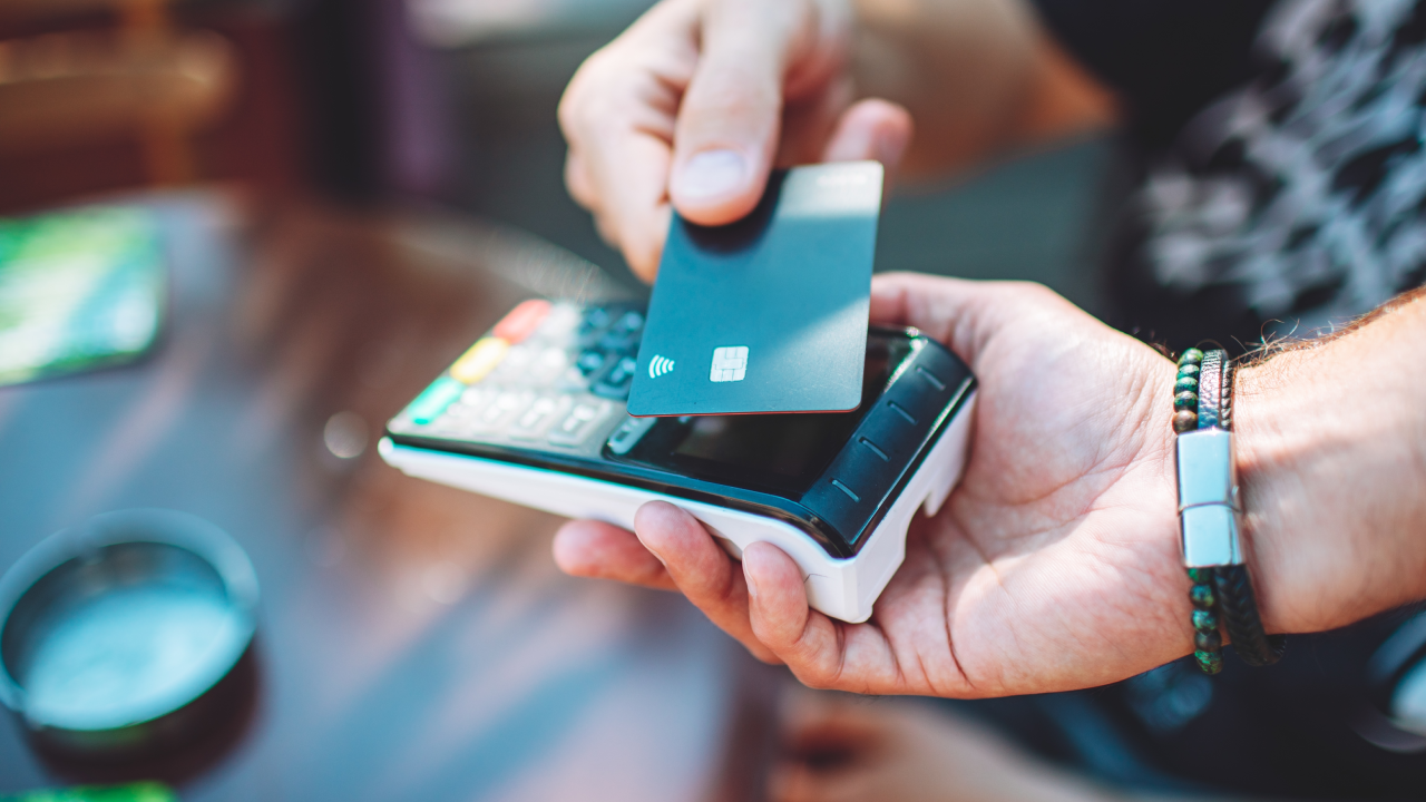 Adult man paying with credit card at cafe, close-up of hands with credit card and credit card reader