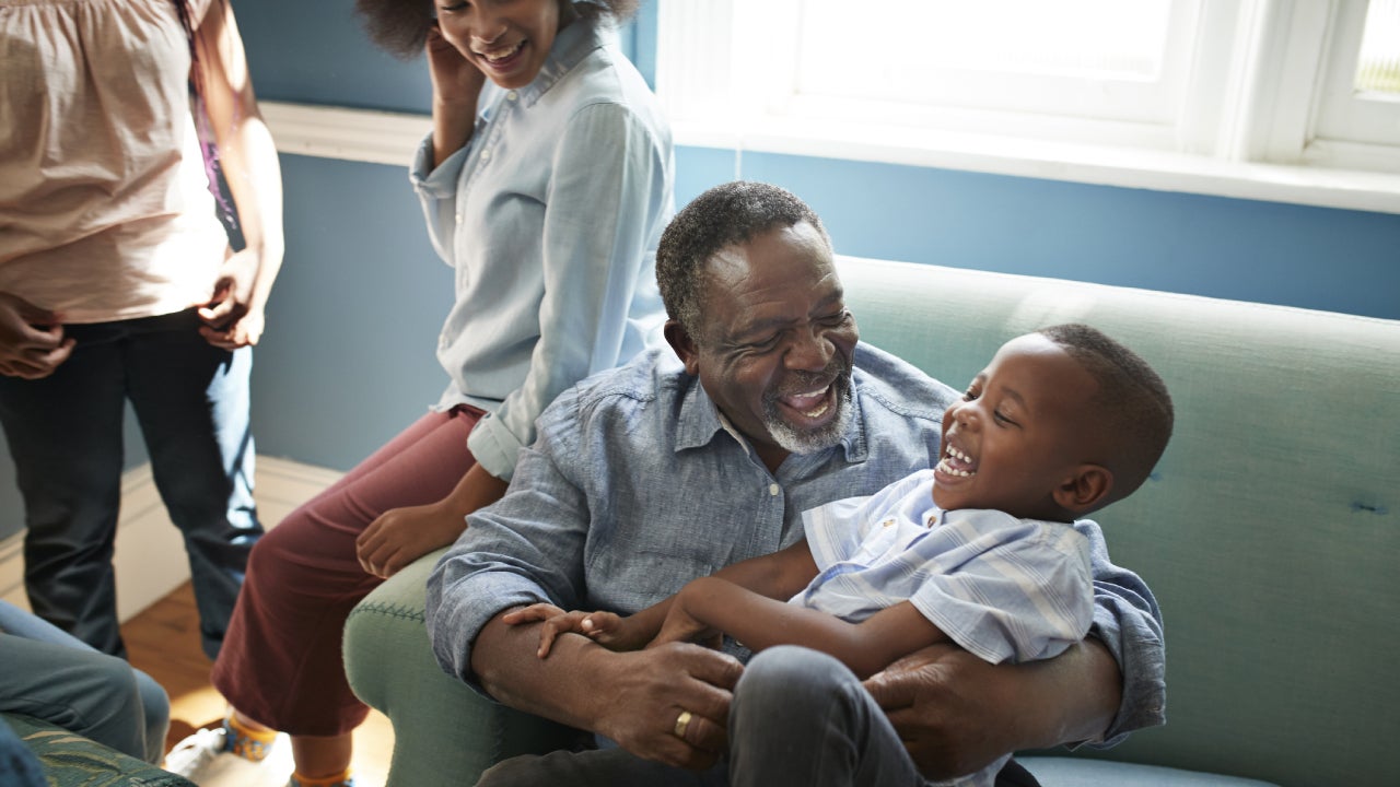 A grandpa plays with his grandson in the living room while the family looks on.