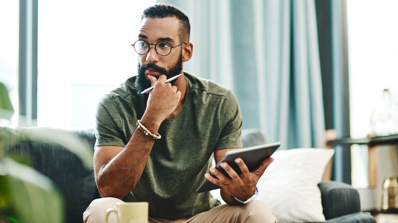 A man sits with a tablet looking pensive