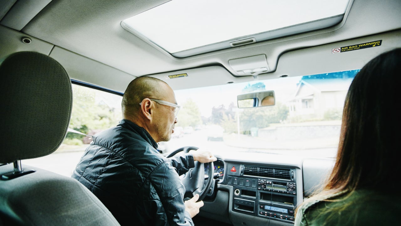 Older Asian man drives his car with his daughter in the passenger seat.