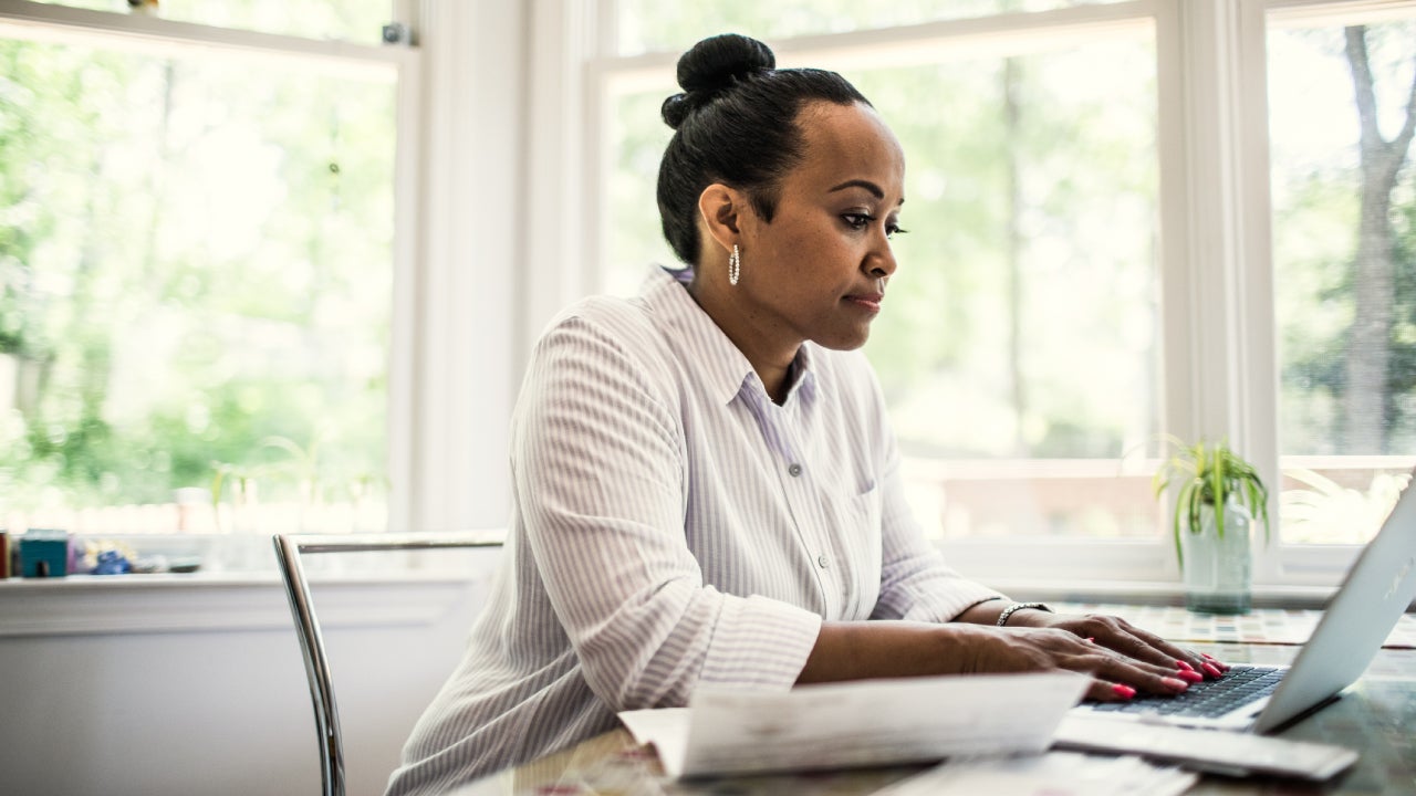 A black woman with her hair done up in a bun sitting at her desk in front of a laptop.