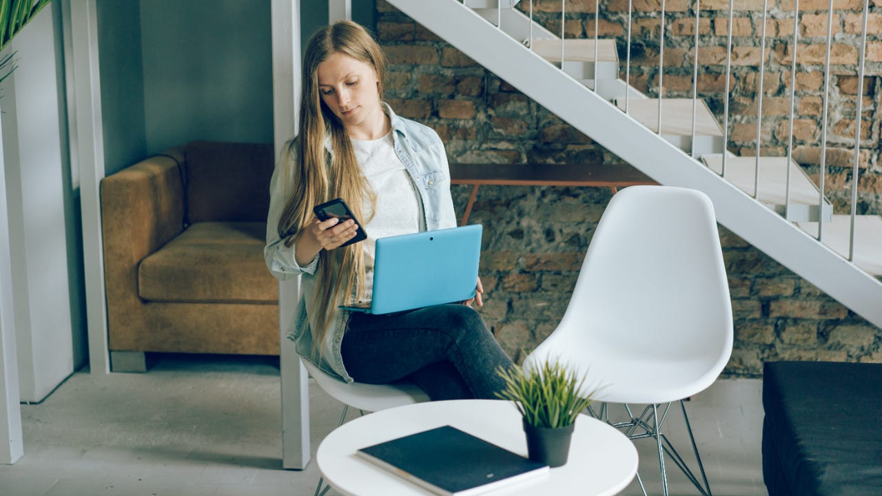 A lady uses her phone and laptop.