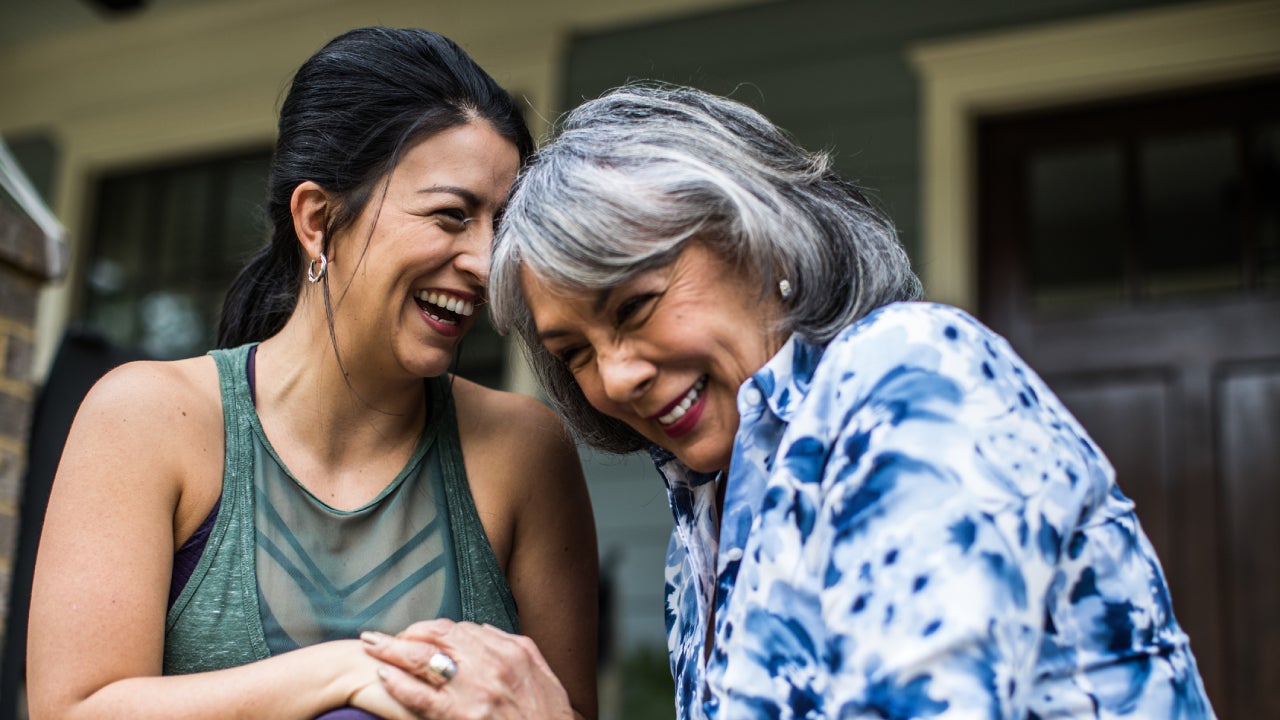 Adult daughter sits with her mother on the porch and are laughing together.