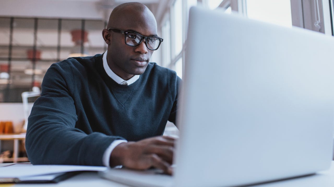 Man with glasses sitting at desk using laptop