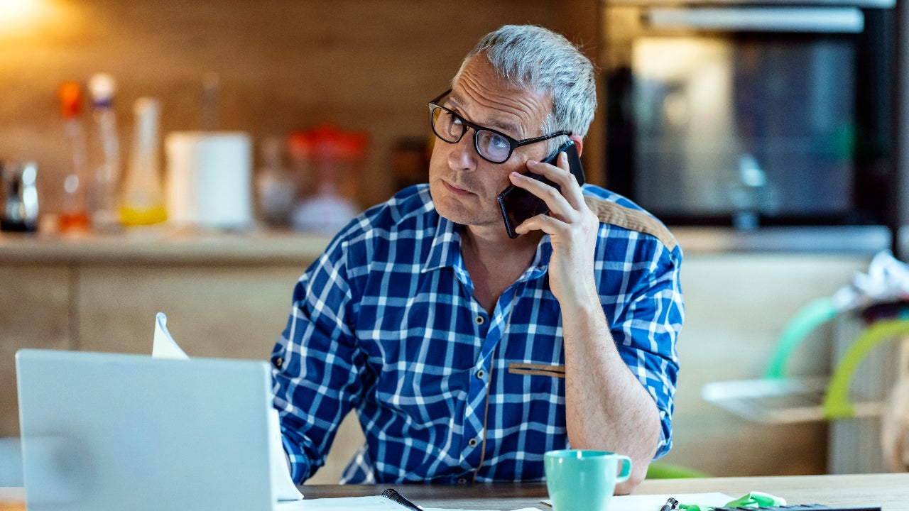 A middle-aged man talks on the phone at his home