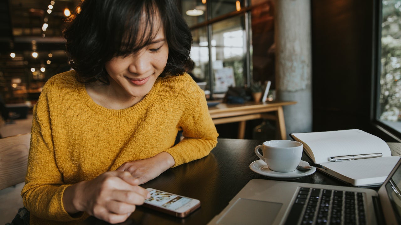 A young woman researches on her phone at a cafe.