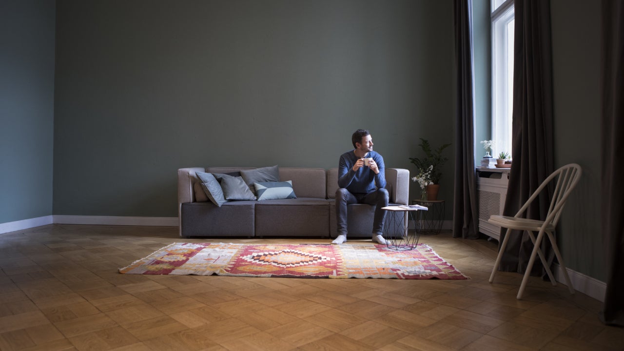 Man sitting on couch at home looking through window