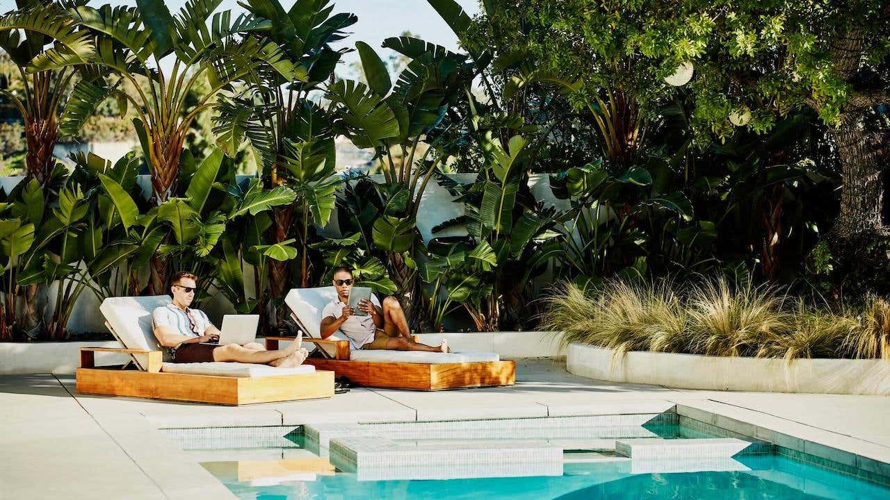 Gay couple working on laptop and digital tablet while relaxing by pool