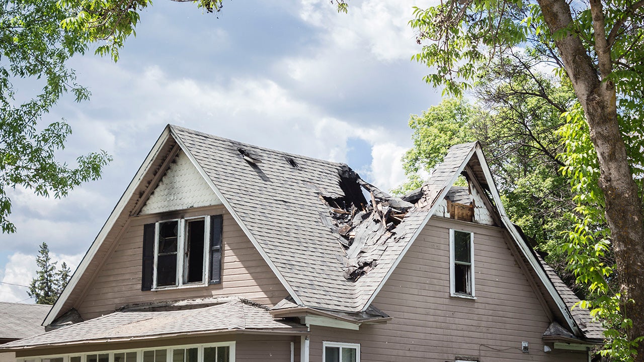 Clear sky after a storm with a house in the foreground. The roof has been severely damaged in the picture.