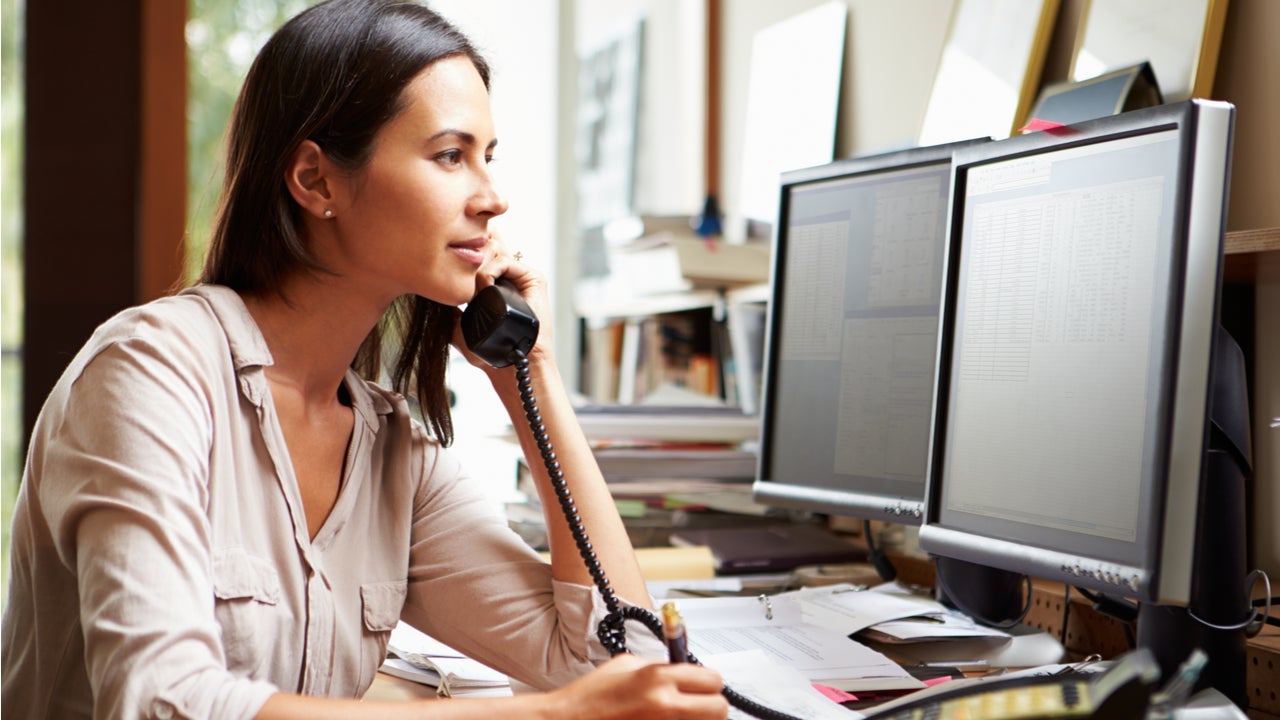 Woman speaks on the phone while looking at computer monitors