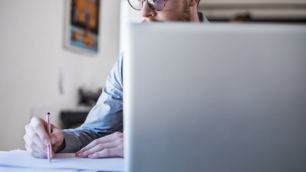 Businessman writing notes at laptop desk