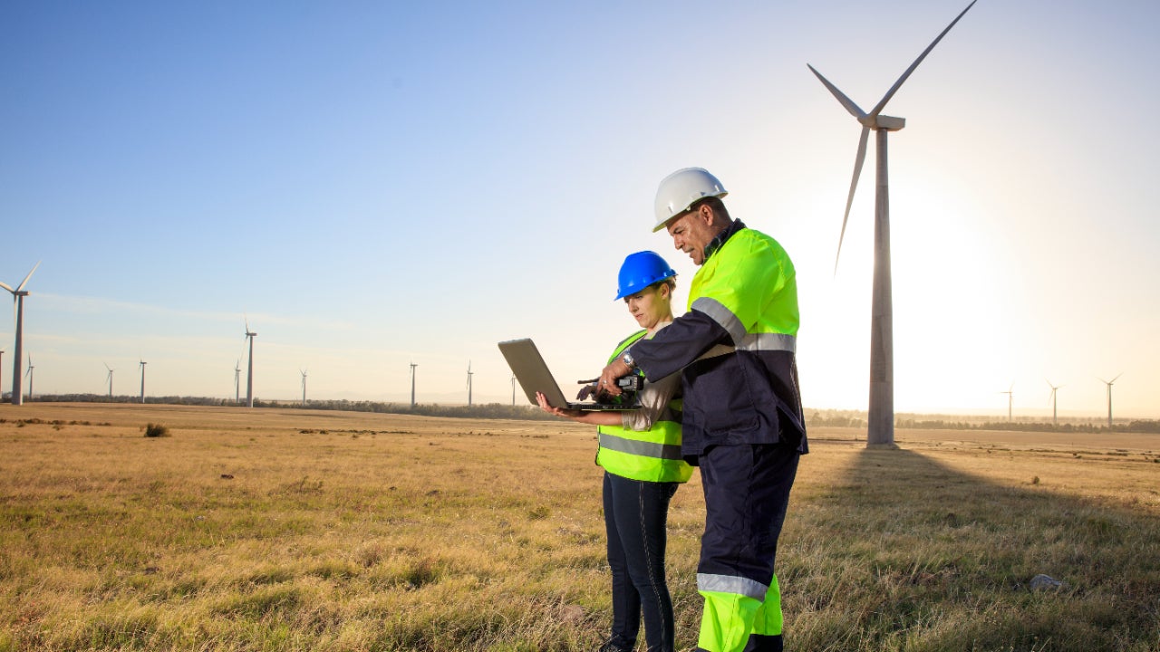 Two engineers stand in a field of windmills