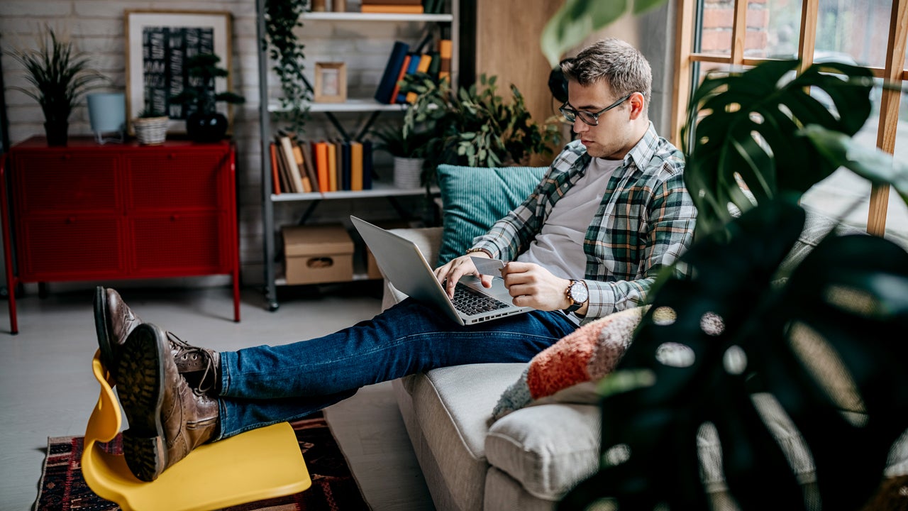 man using a laptop and credit card on the sofa at home