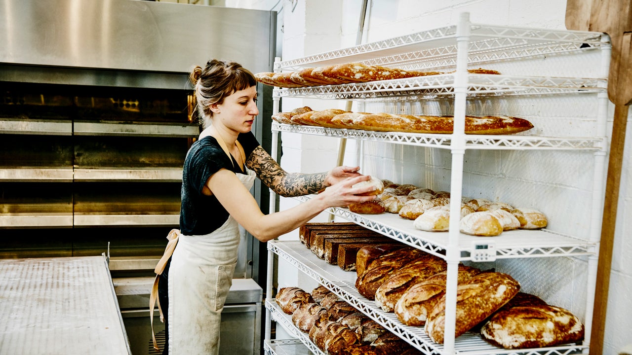 female baker placing bread to cool on a rack in bakery