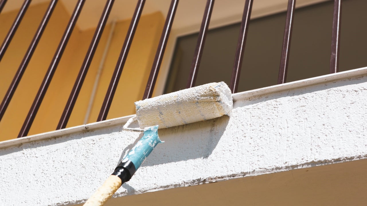 A closeup of a paint roller painting the exterior of a home