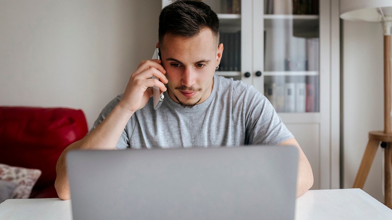 young man talking on the phone at home while using a computer