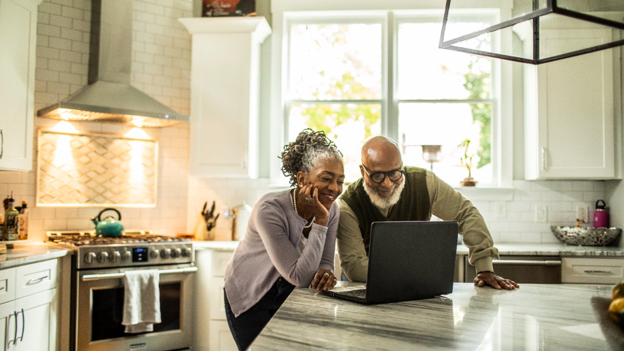 An older couple looks at a laptop computer in their kitchen