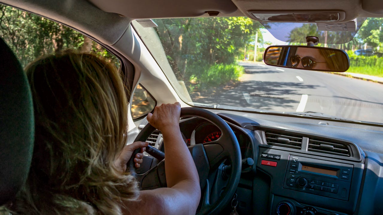 Person driving her car. Over-the-shoulder view where we see no traffic in front of her.