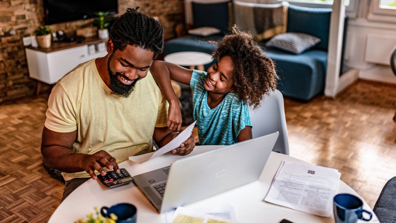 father working on finances with his daughter sitting next to him