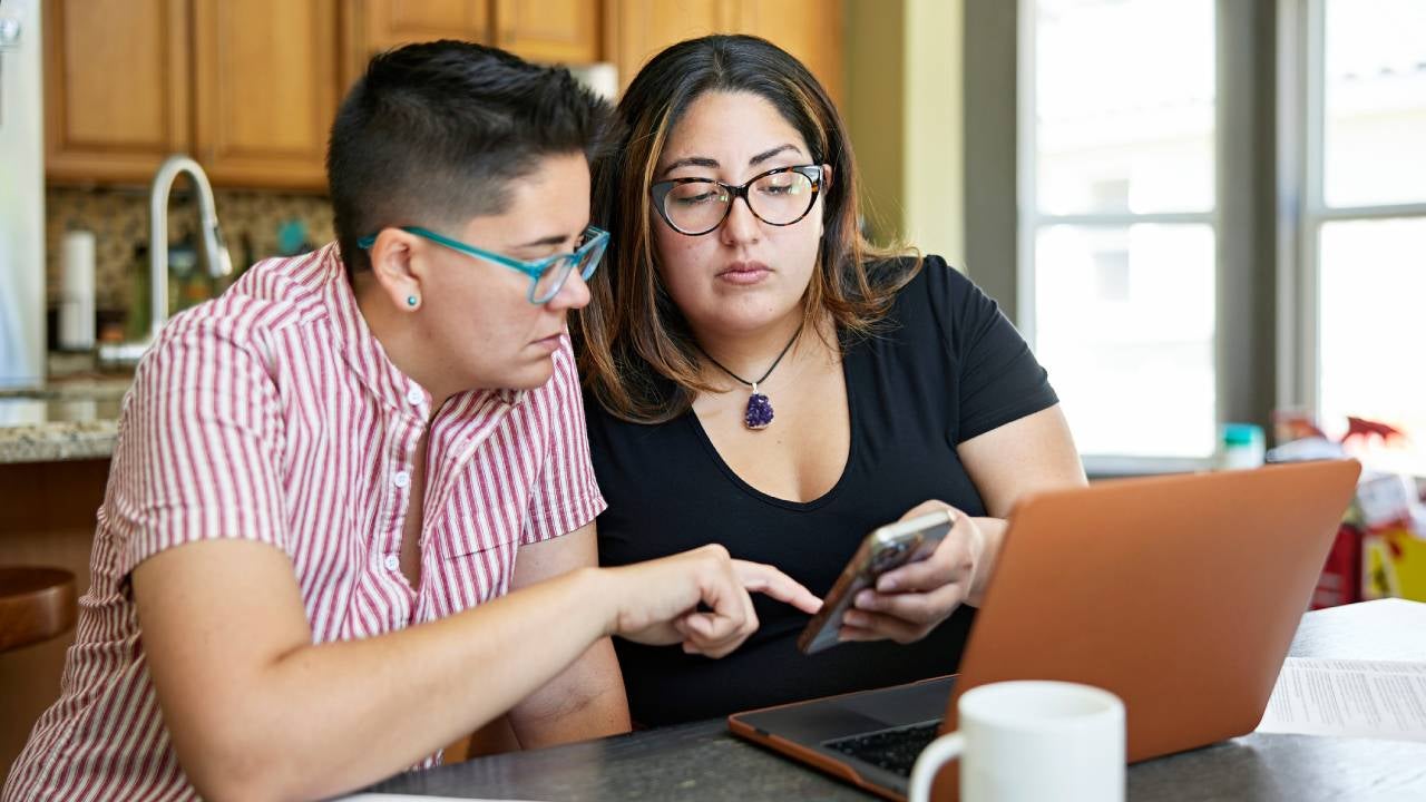 Two people sitting together in family home with paperwork, laptop, and making calculations on smart phone