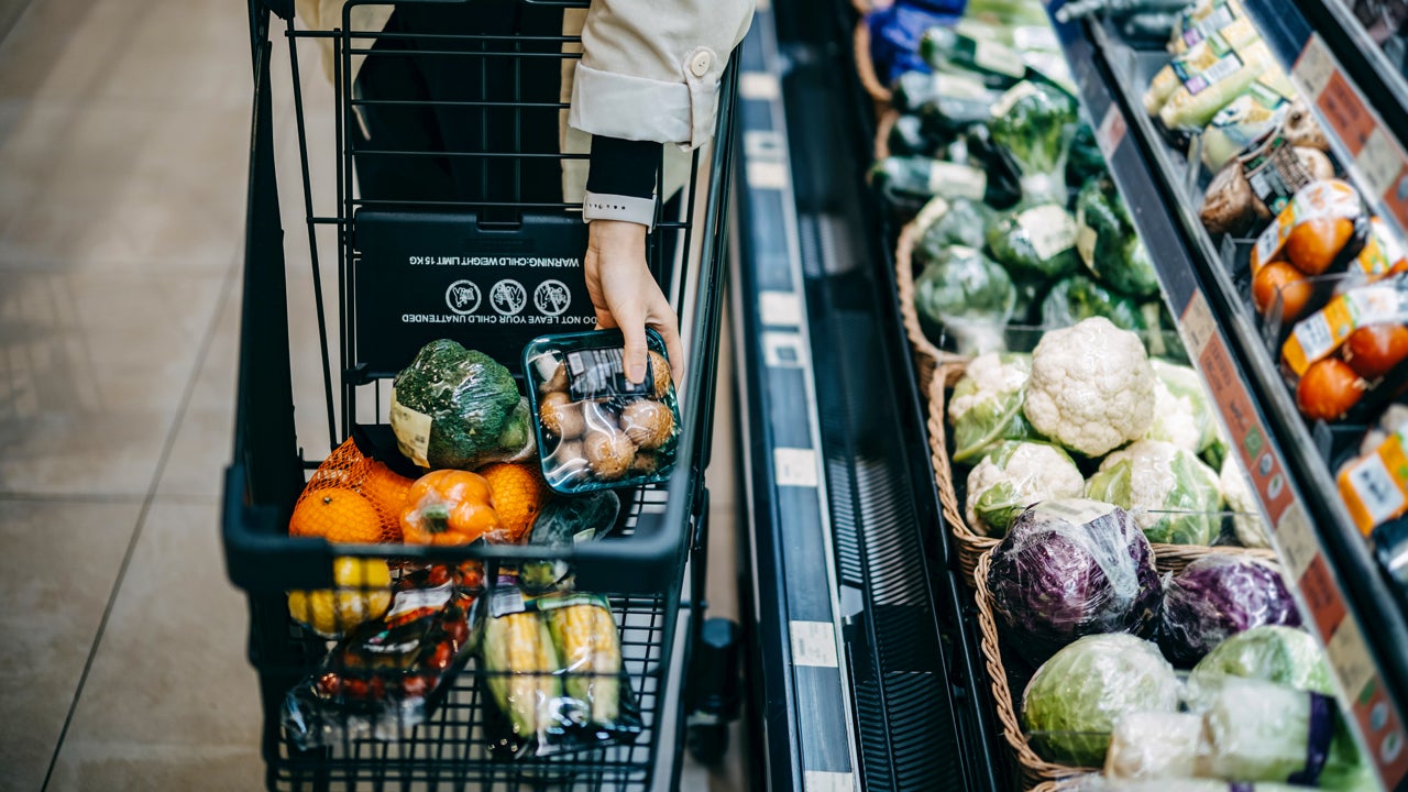 a close up shot of person filling up a grocery cart next to produce section at a store