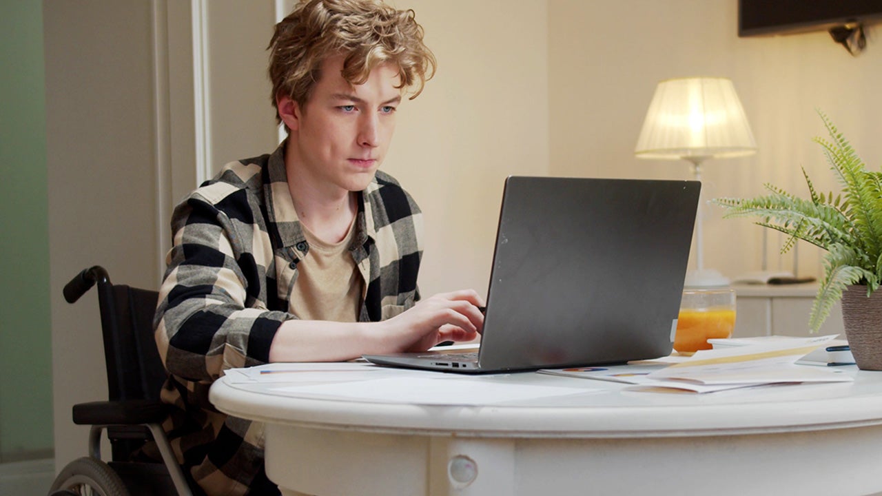 Young Man Sitting On Wheelchair Using Laptop