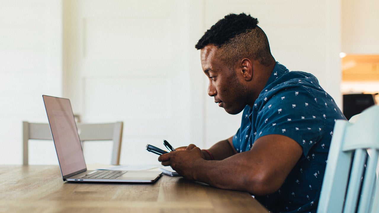 man sitting at a table and looking at his laptop and phone