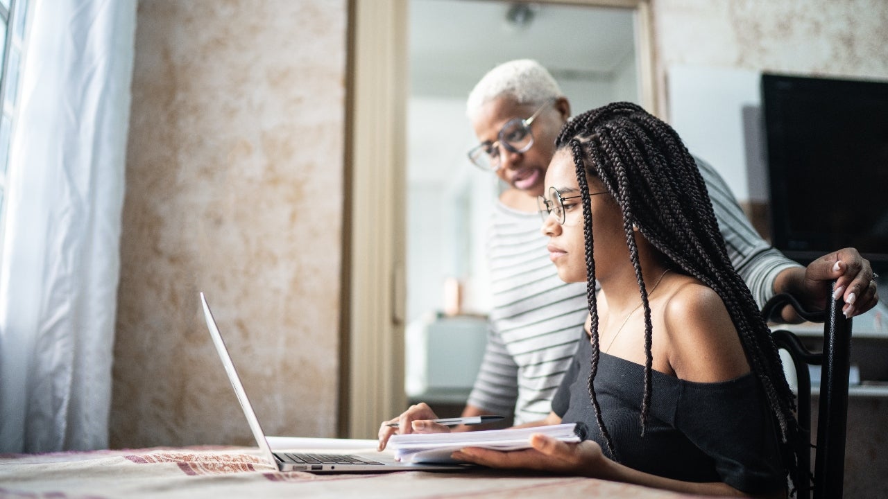 Woman looks over young student's shoulder at laptop