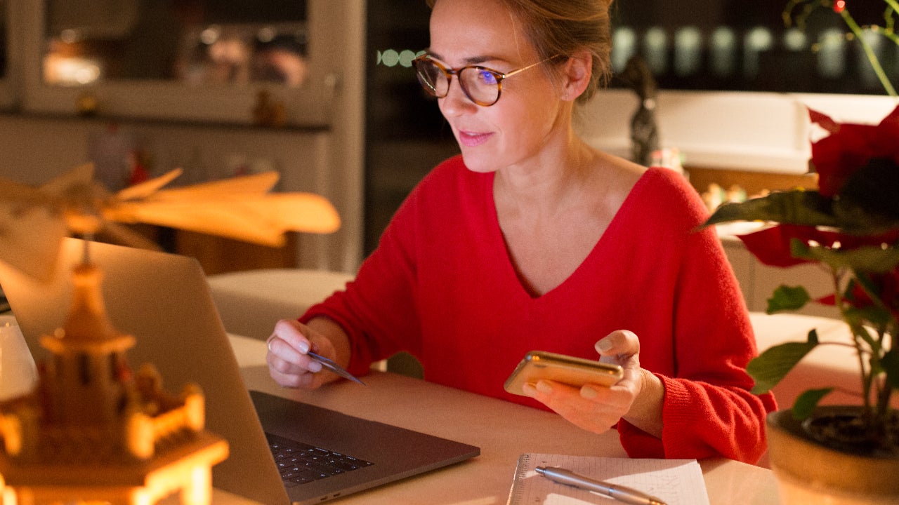 Woman wearing glasses on laptop while holding phone