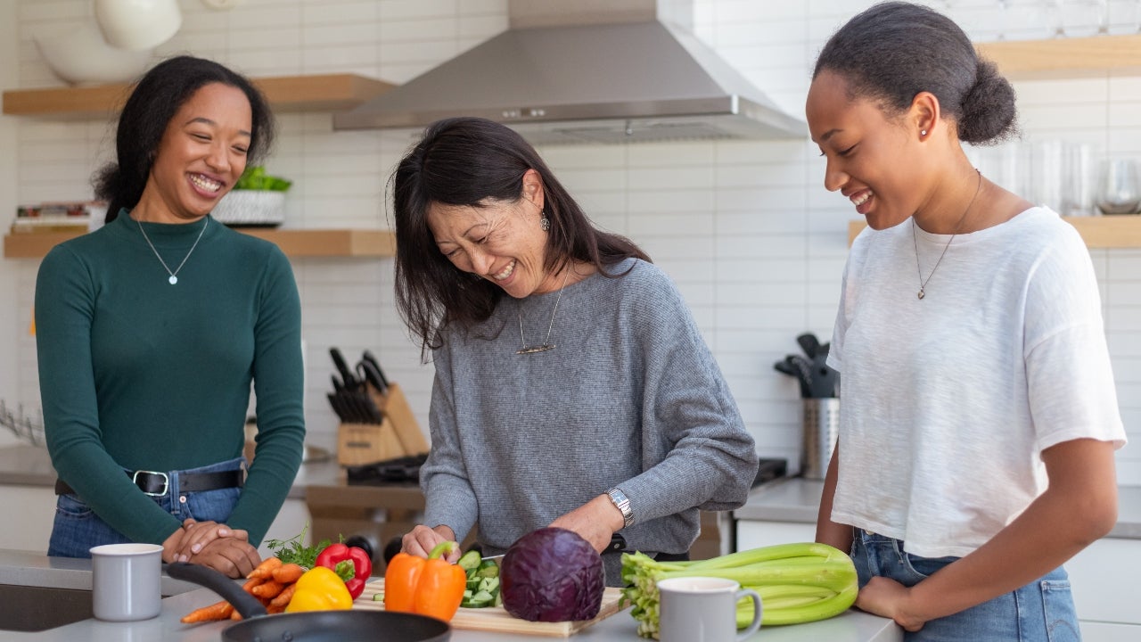 Two high school girls cook with mother in kitchen