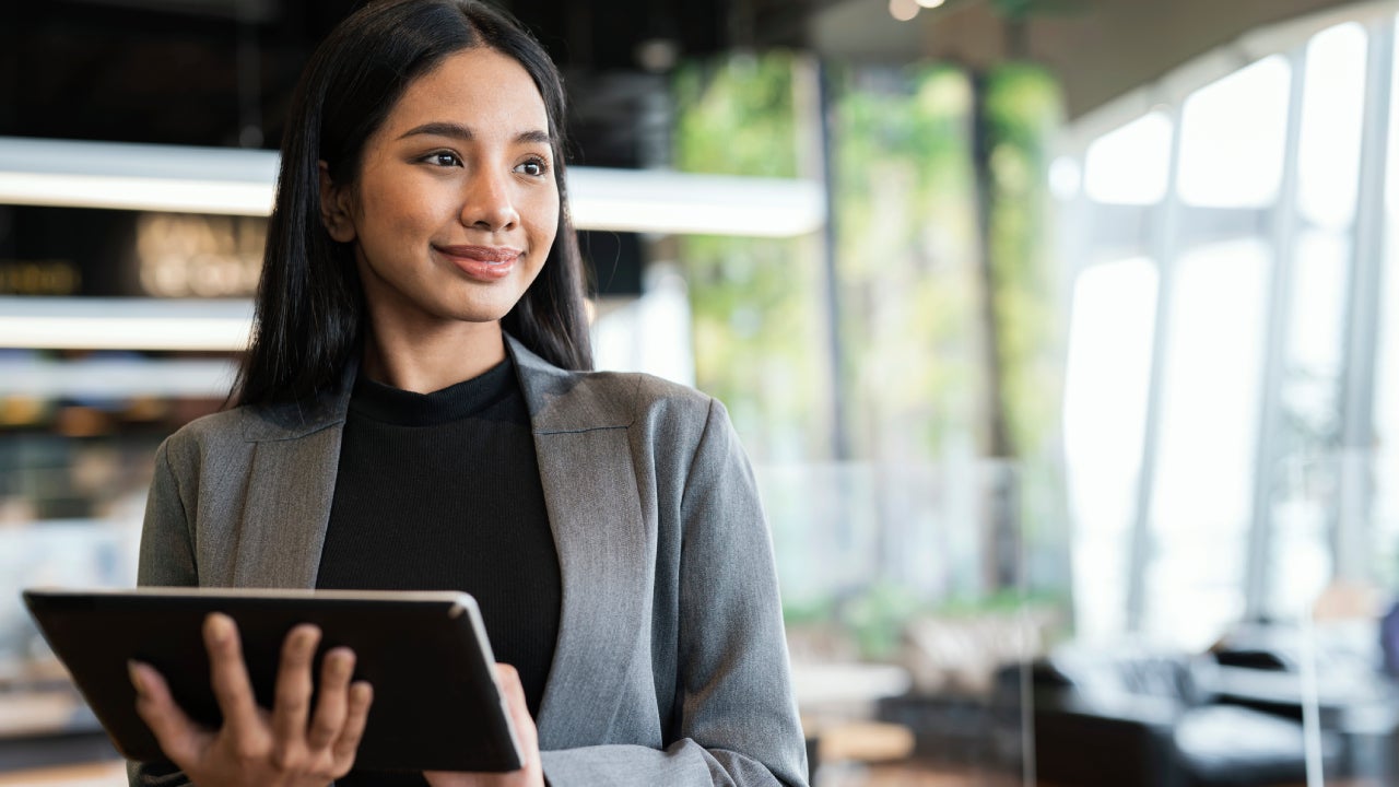 Portrait of a Young Businesswomen using a tablet while standing and looking away in a financial business office