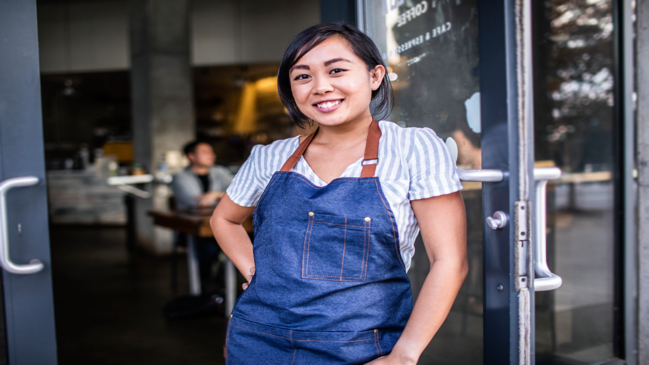 Asian woman wearing apron outside of storefront