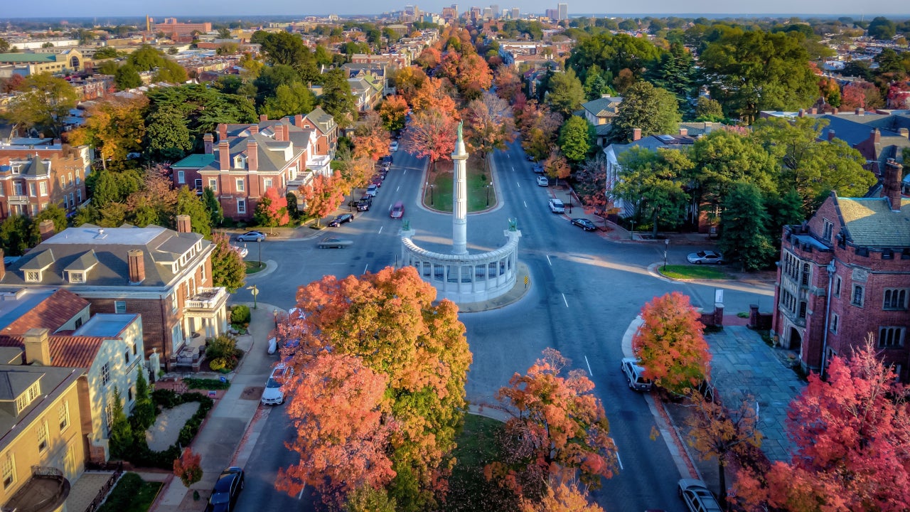 An aerial view above beautiful Fall foliage on Monument Avenue and the skyline of Richmond Virginia in the distance.