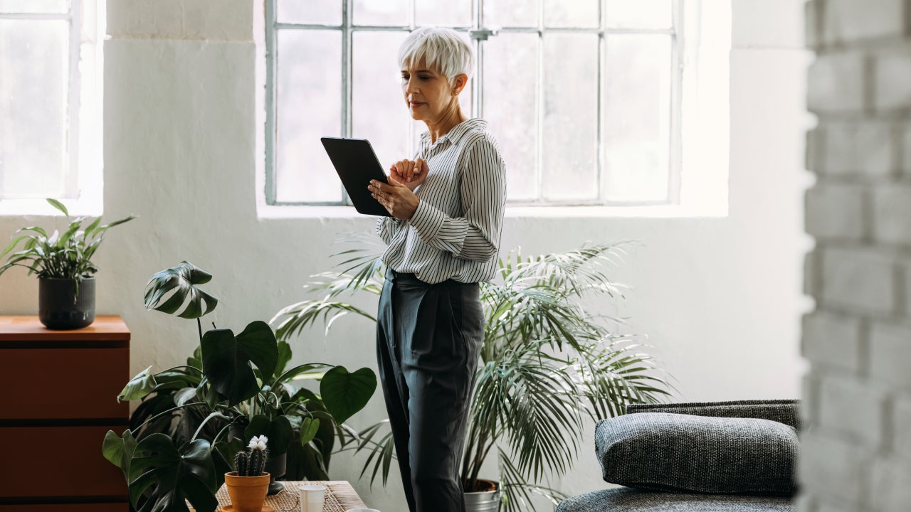 Serious businesswoman reading business report on her tablet while standing in a living room.