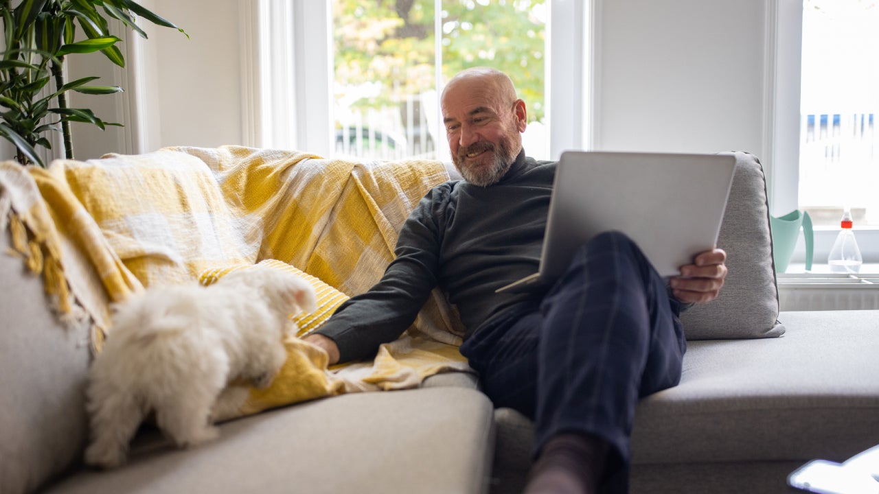 man using laptop, while petting Maltese dog