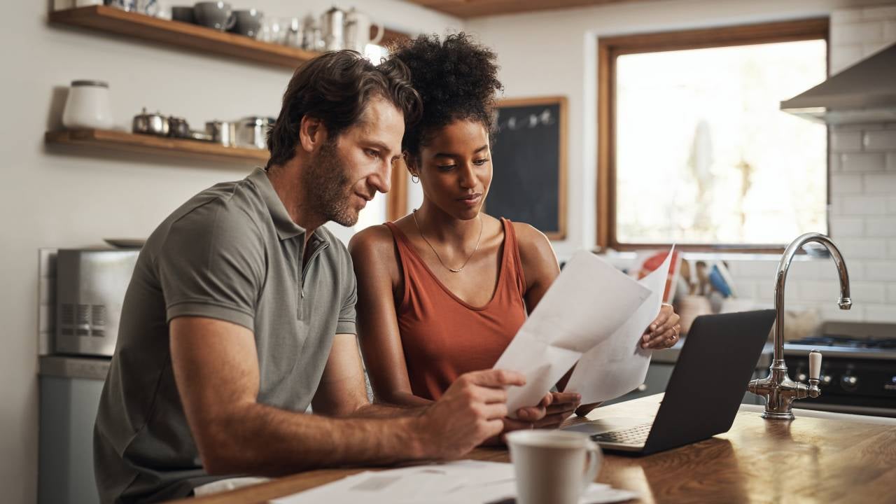 Cropped shot of a couple using their laptop and going through paperwork at home