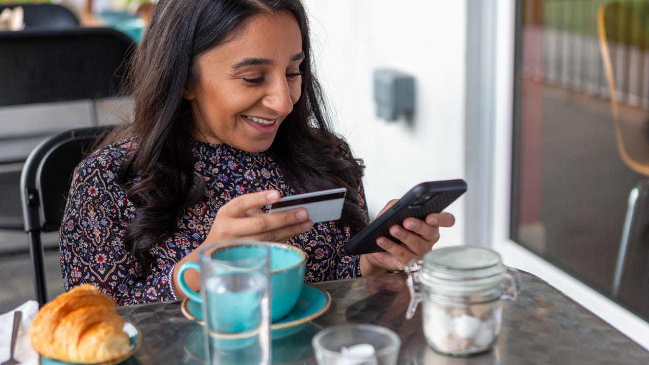 Smiling woman making online payment with credit card in cafe