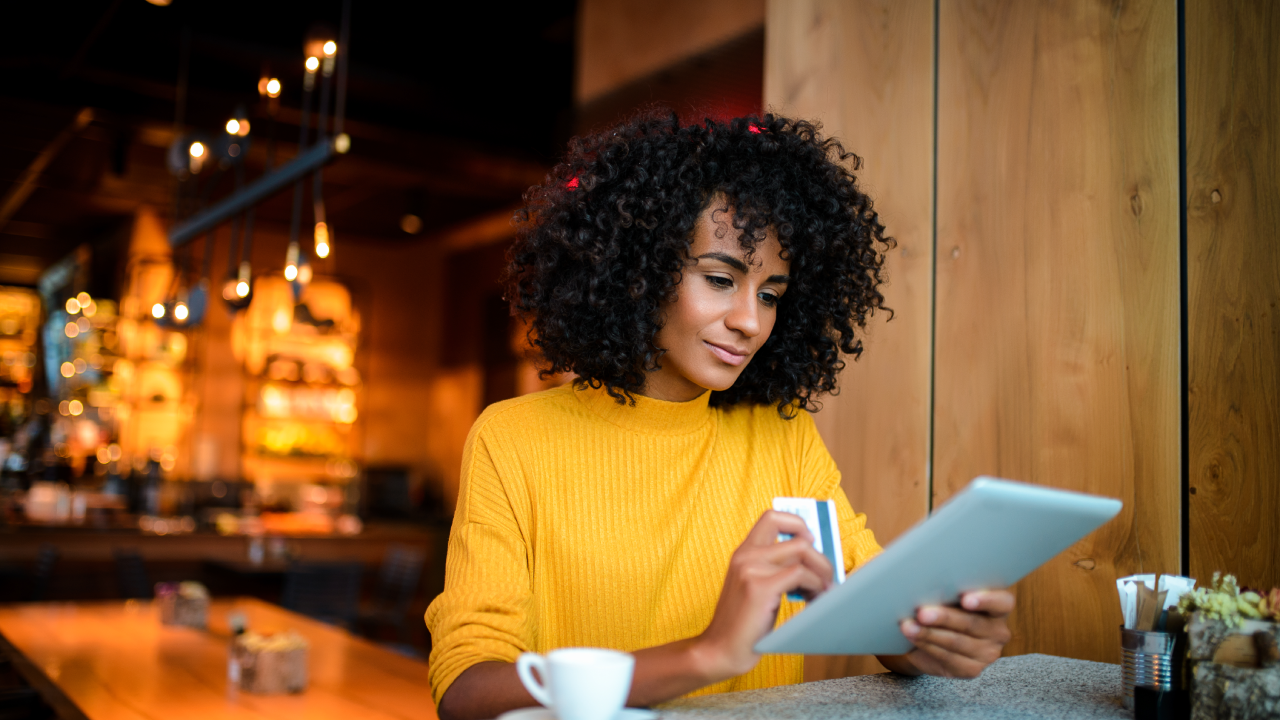 Beautiful smiling African American woman using digital tablet at the bar.