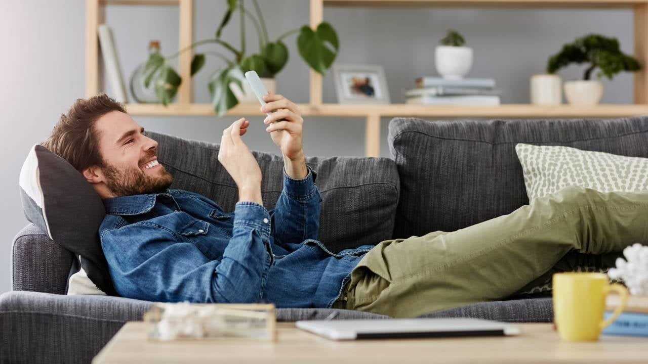 Shot of a young man using his mobile phone while laying on his couch at home