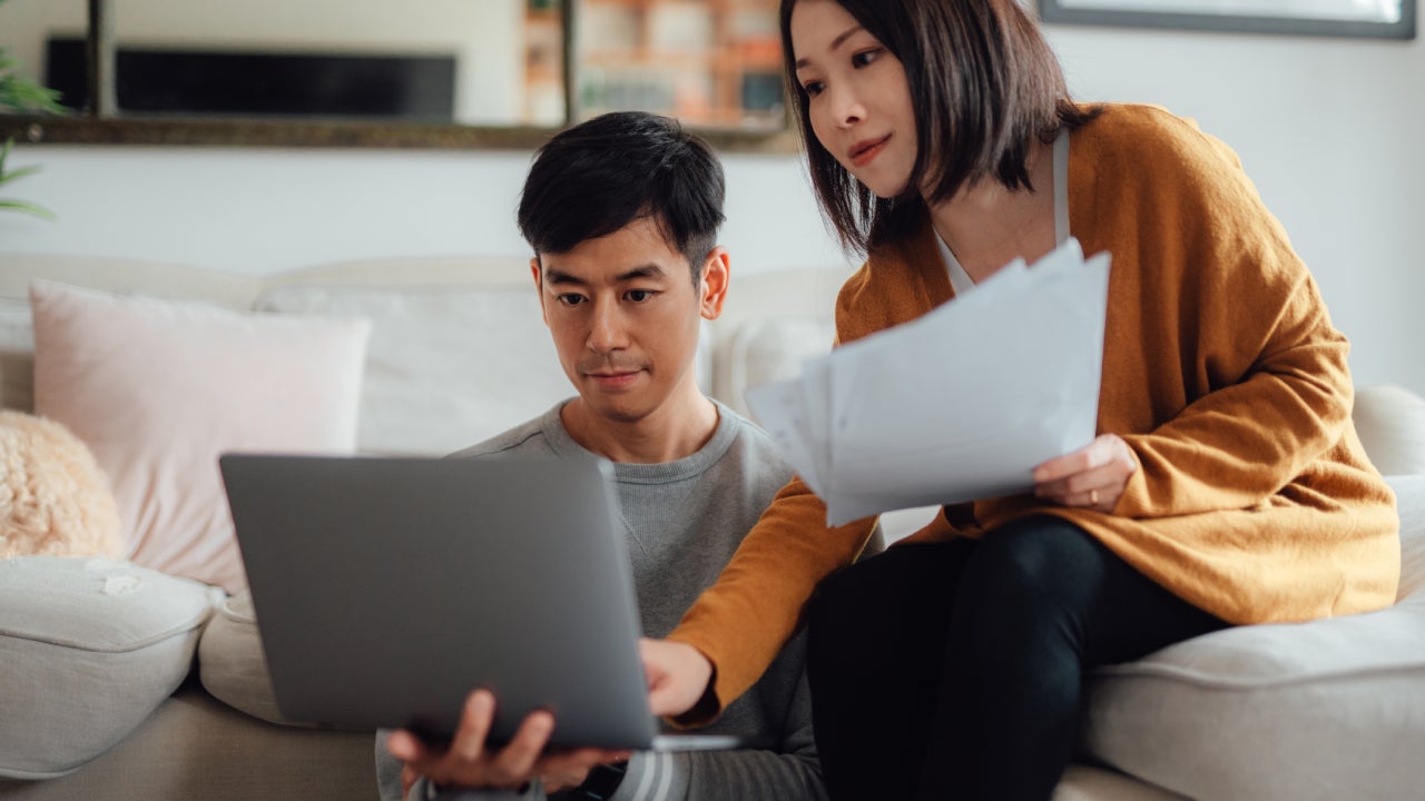 Serious looking young couple discussing over financial bills while using laptop in living room. Couple paying bills together online. Making financial plan together. Doing online banking on laptop, paying taxes, managing personal budgets, discussing finances, managing online stock trades, making college tuition planning for children...