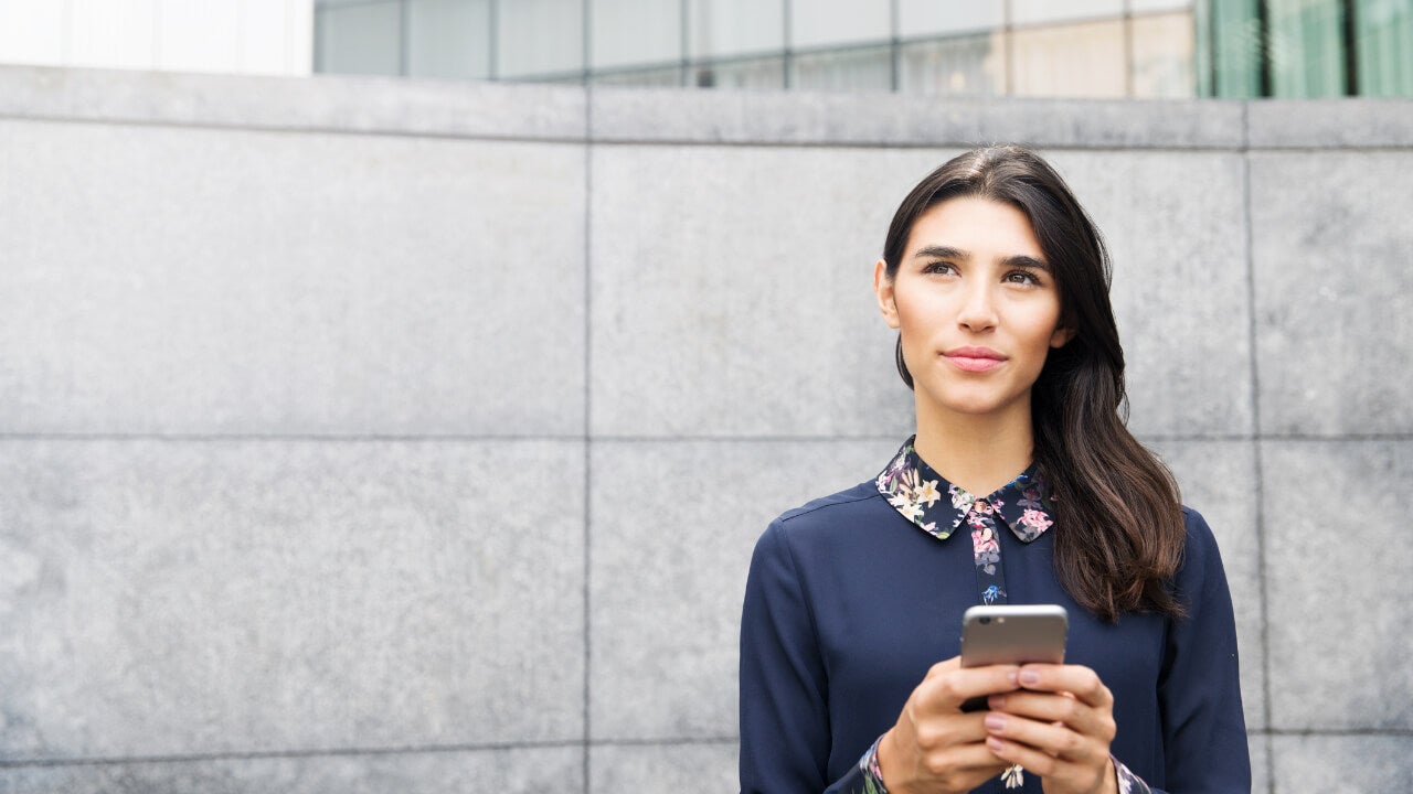 A woman holding a phone looks pensively into the distance.