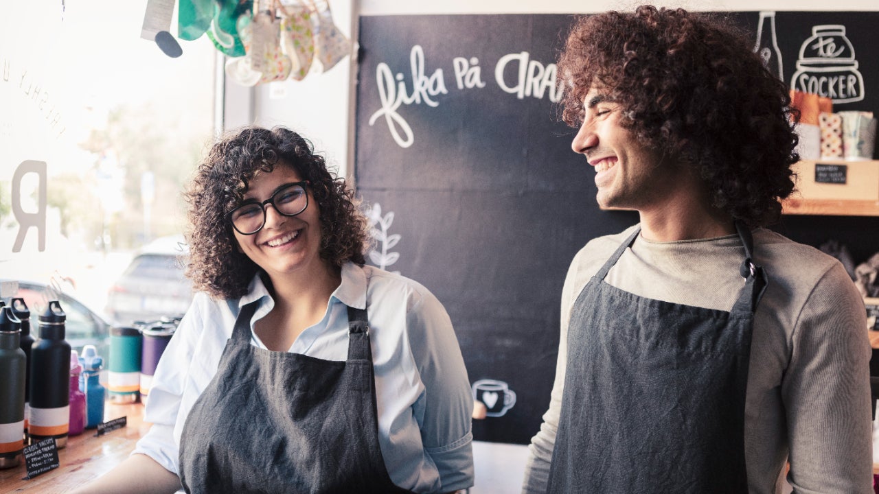 Male and female co-owners work together in aprons at a shop.