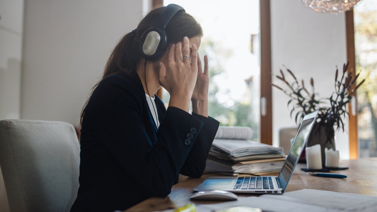 Stressed woman rubbing temples while looking at laptop