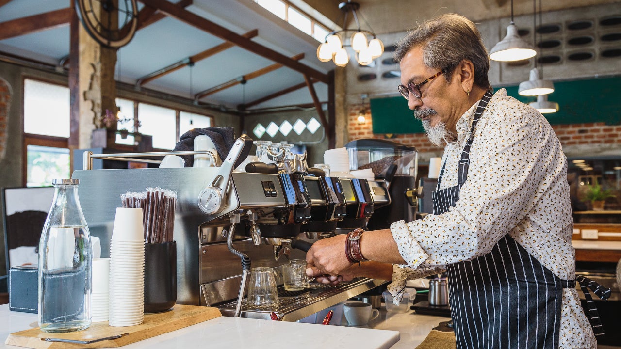 A coffeeshop owner uses his coffee machine at bar counter in cafe.