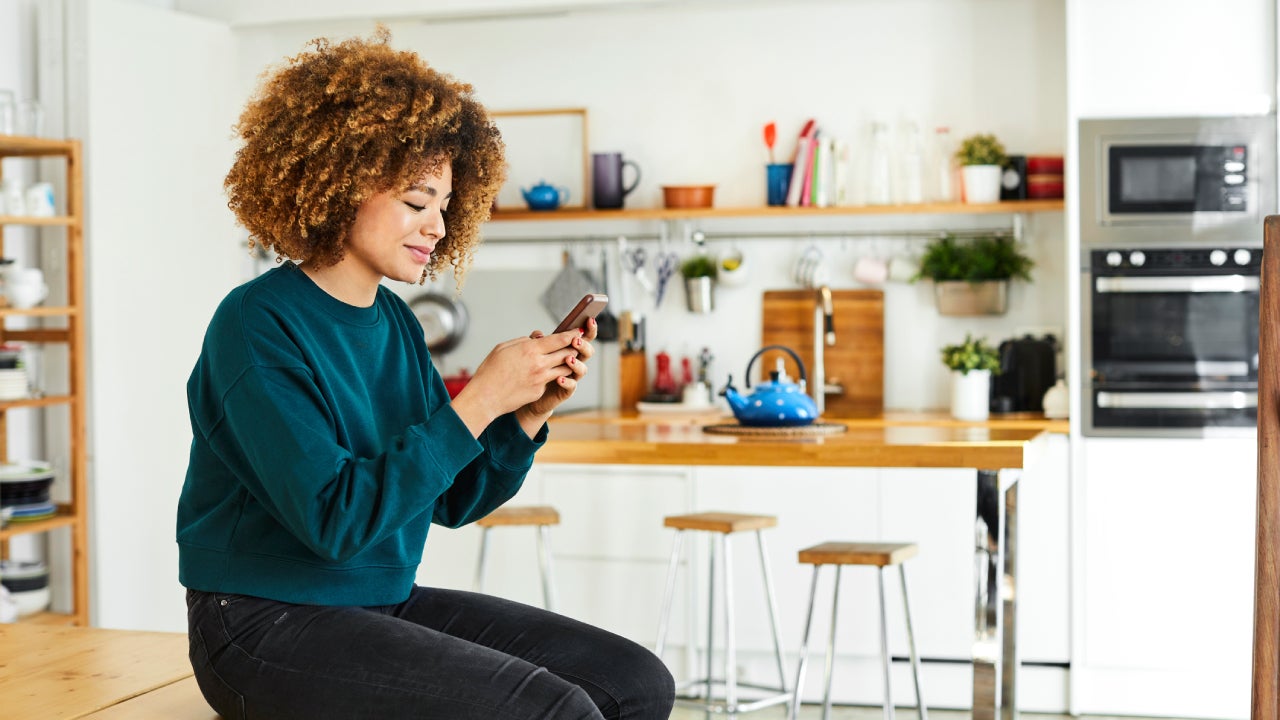 Woman using cell phone and sitting on kitchen counter