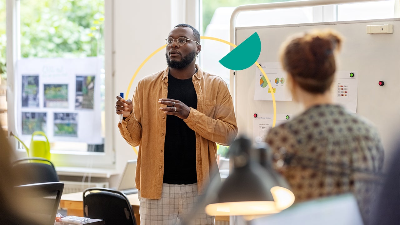 A man speaks with coworkers in front of a whiteboard.