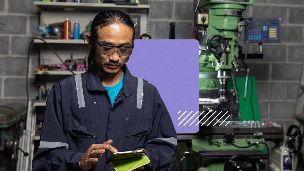 A black man wearing coverals uses a cell phone in a small business.