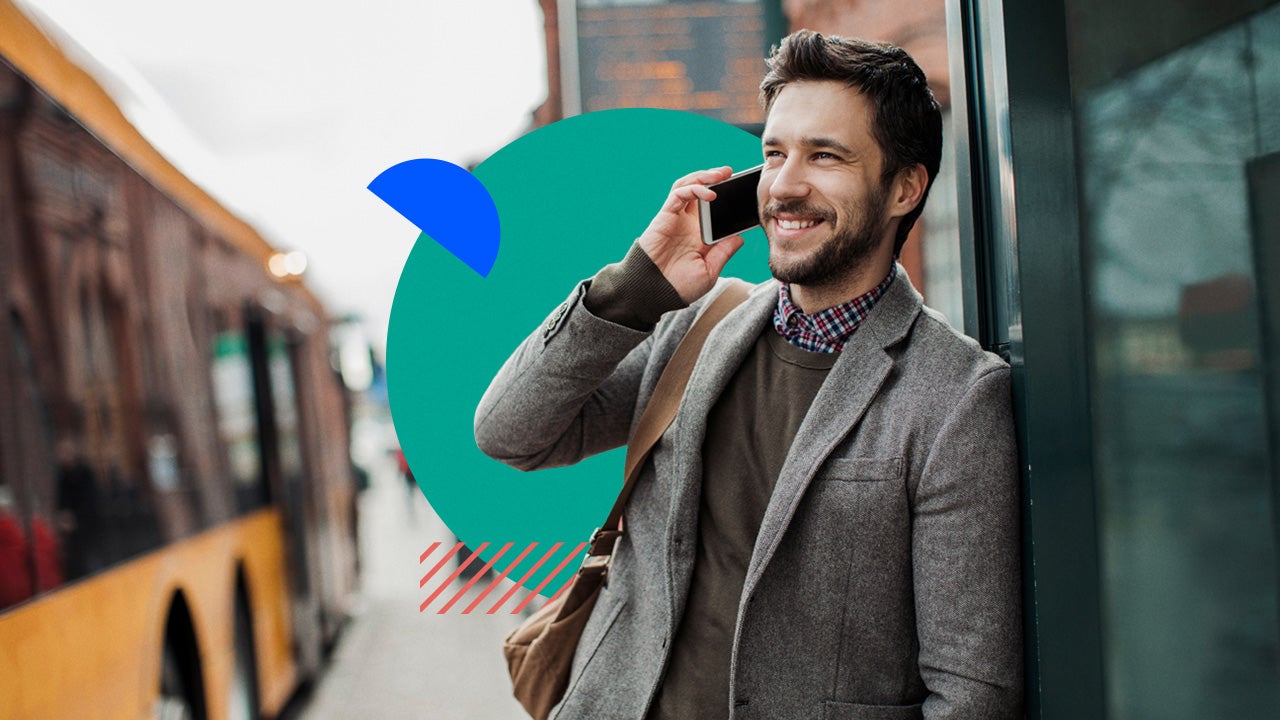 Man in a suit leans against a building, smiling and talking on his phone.